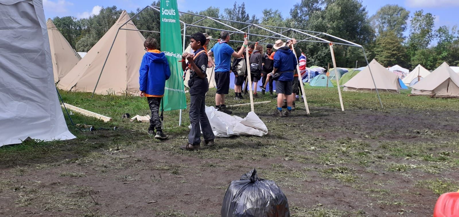 A group of people are standing in a muddy field in front of tents.