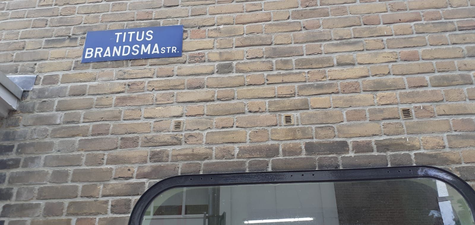 A brick wall with a blue sign that says titus brandsma