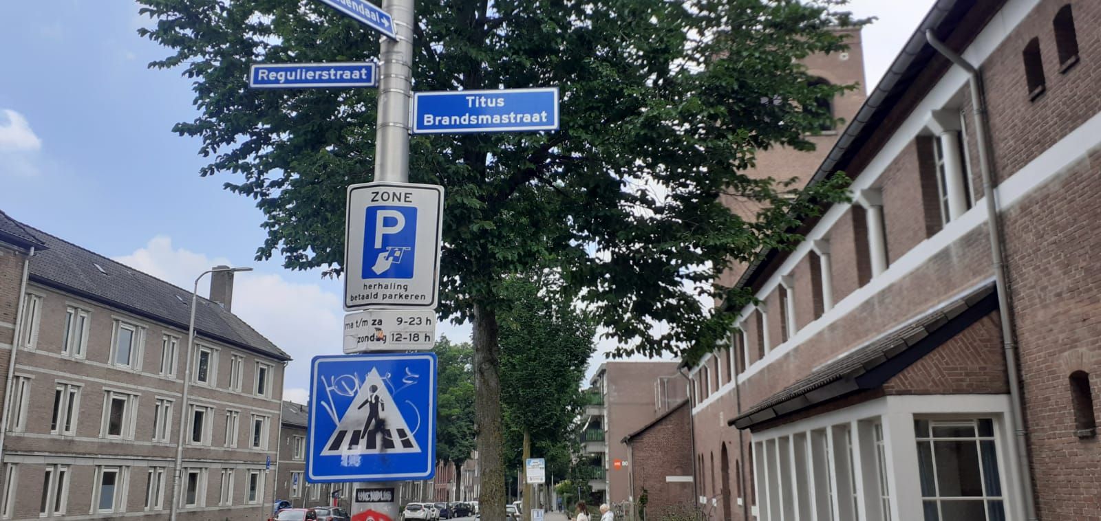 A parking sign is hanging from a pole in the middle of a street.