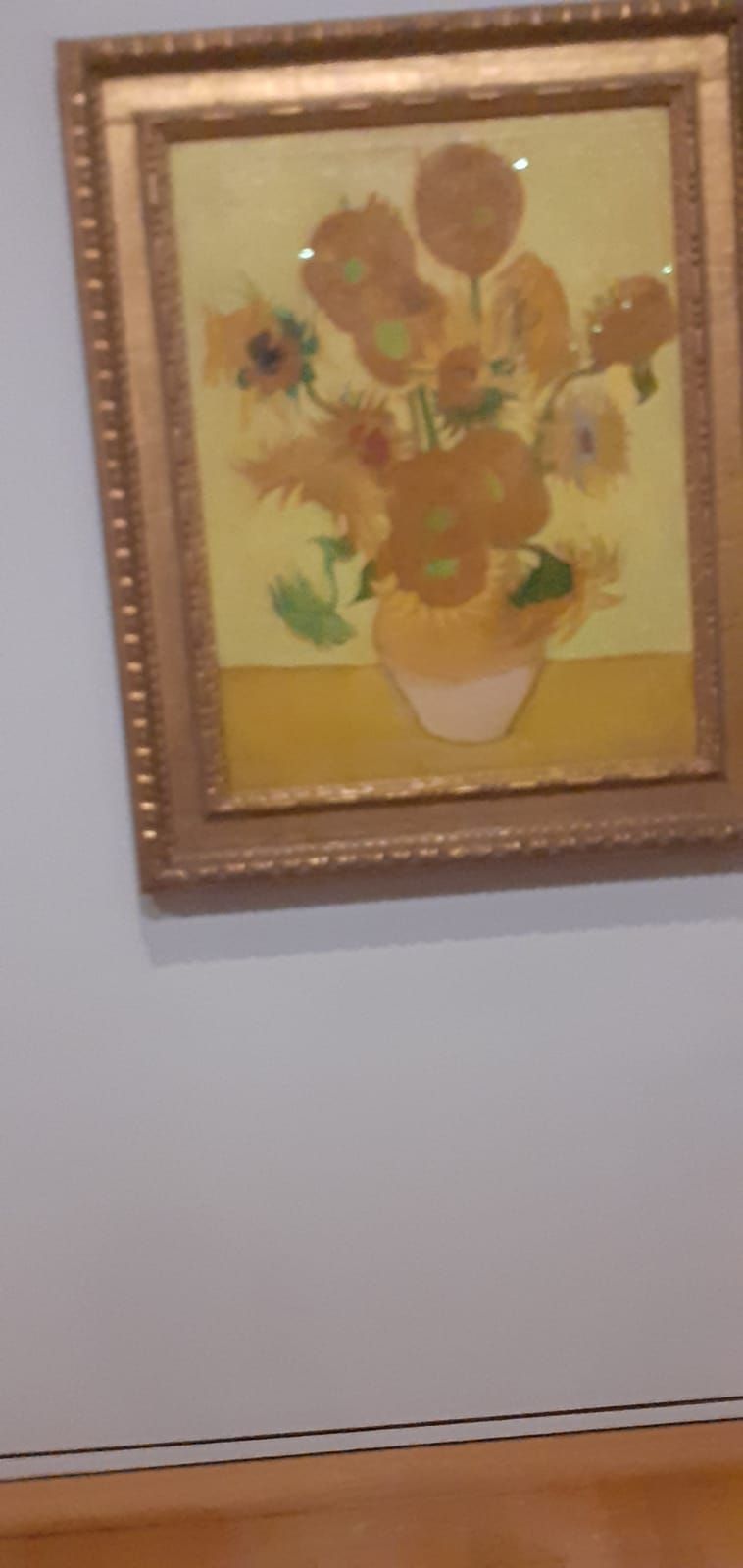 A painting of sunflowers in a vase is hanging on a wall.