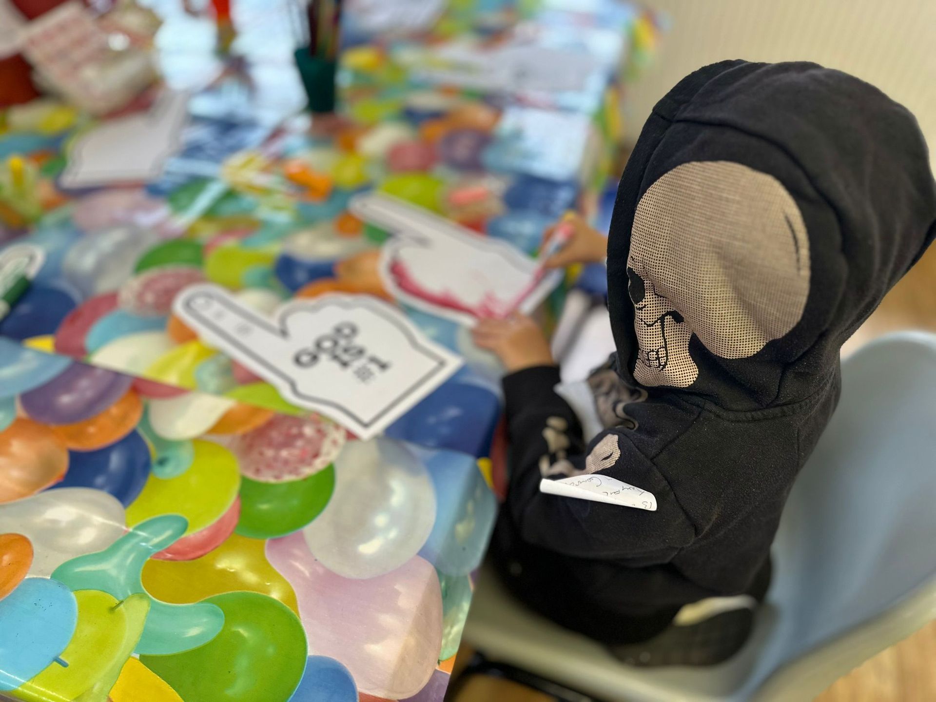 A child dressed as a grim reaper is sitting at a table with balloons.