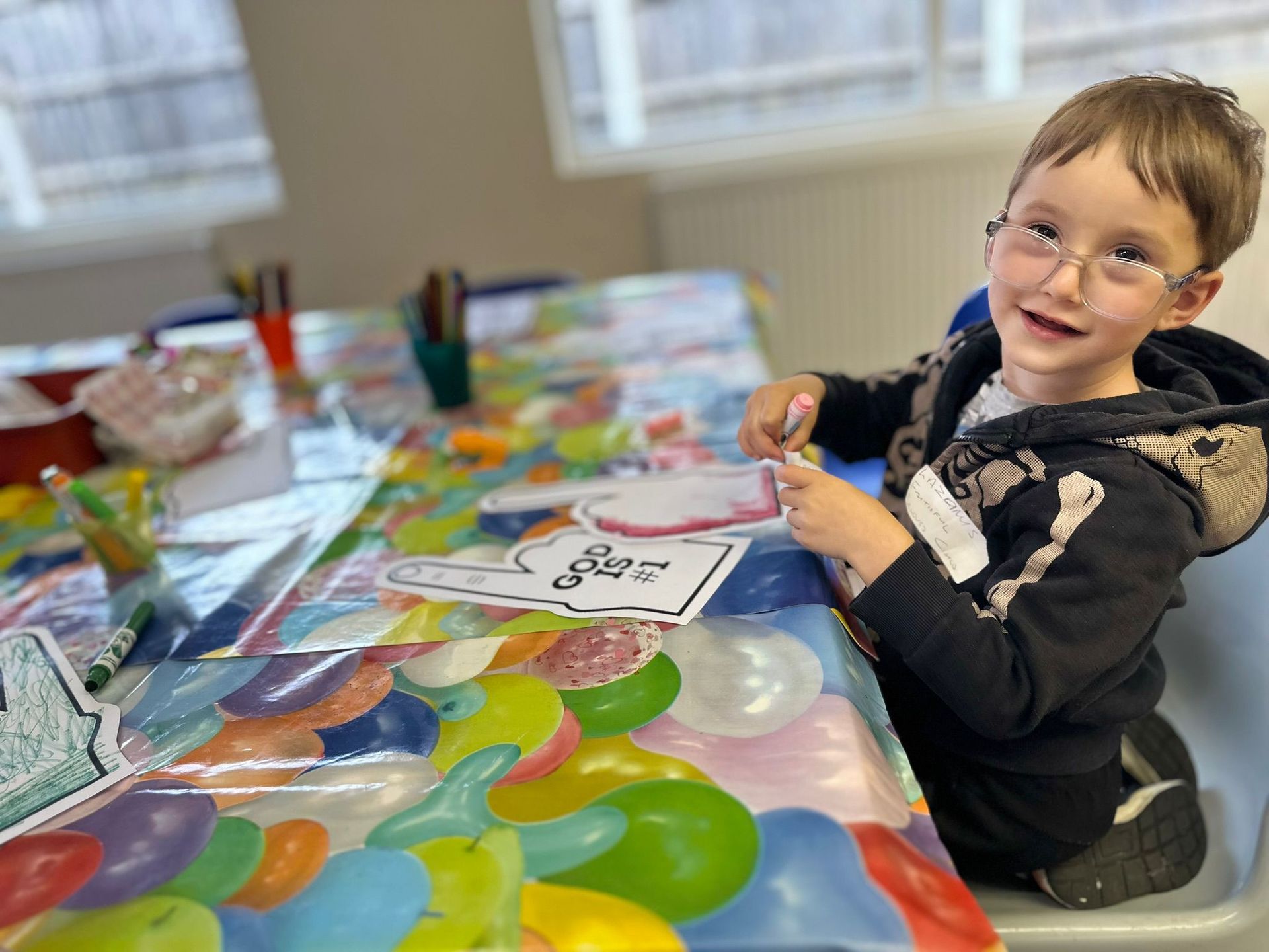 A young boy is sitting at a table with balloons on it.