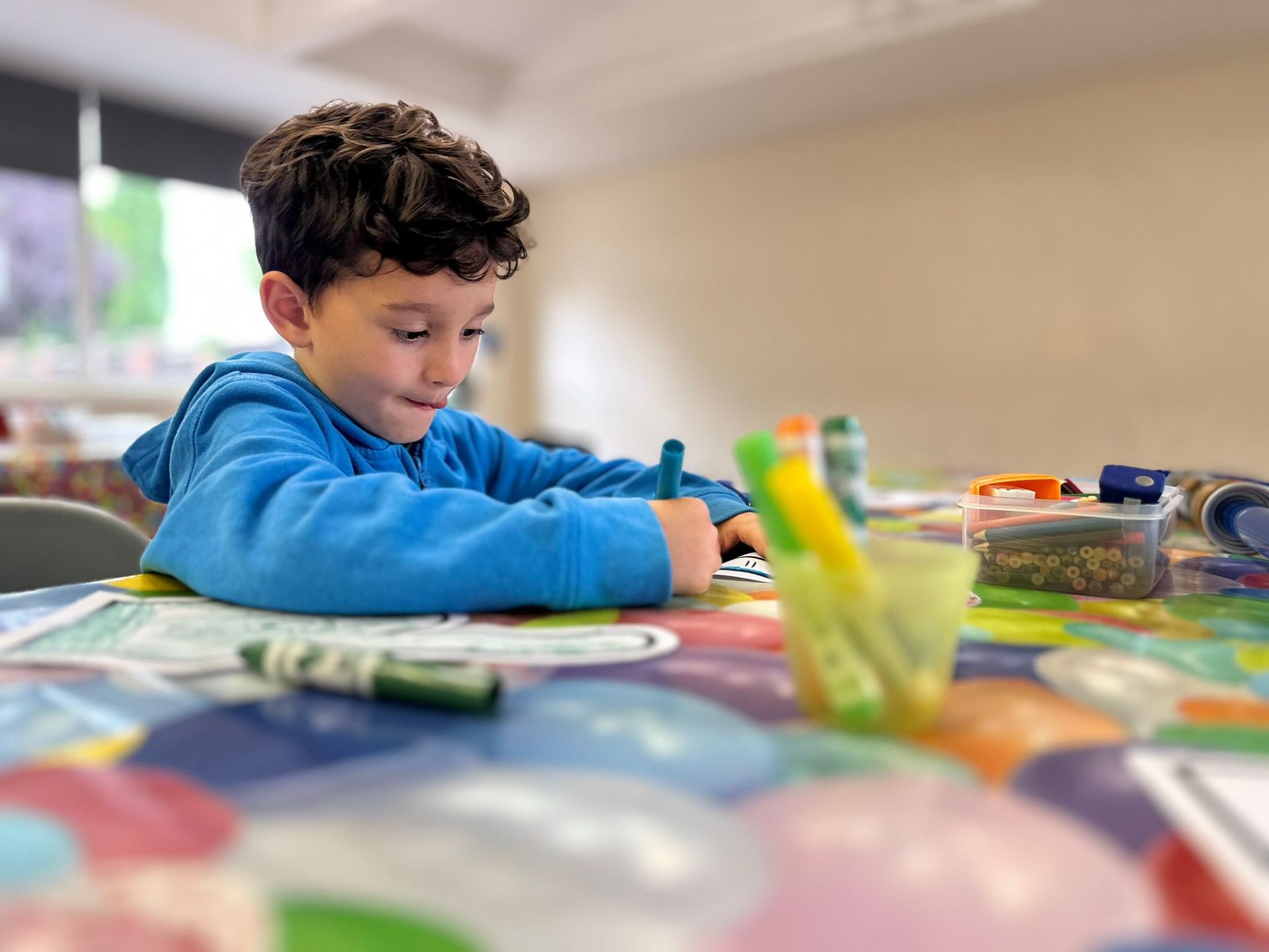A young boy is sitting at a table drawing with markers.