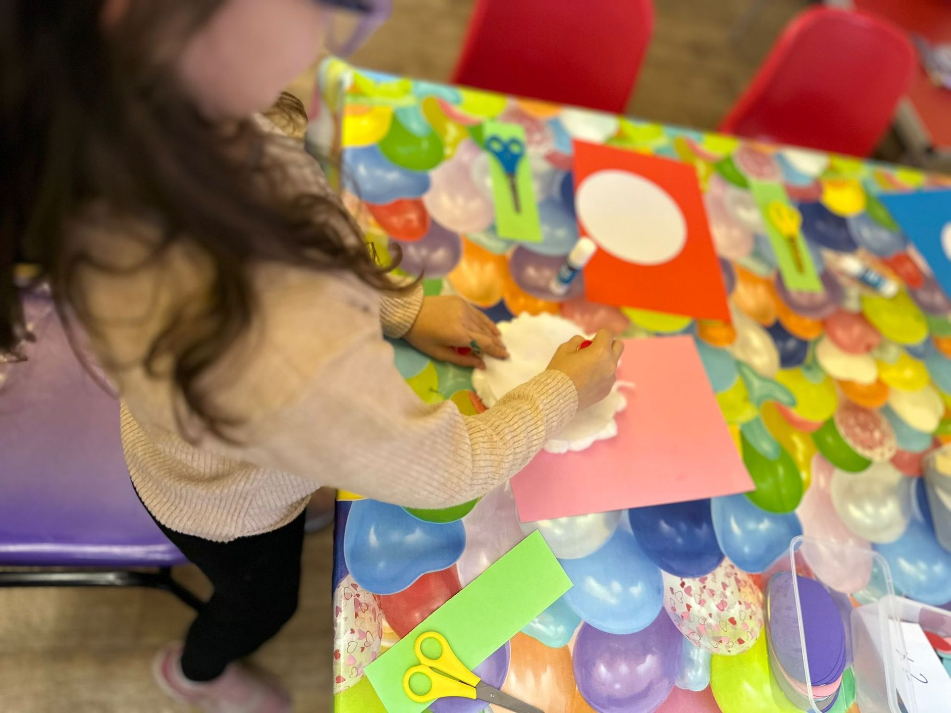 A little girl is sitting at a table cutting paper with scissors.