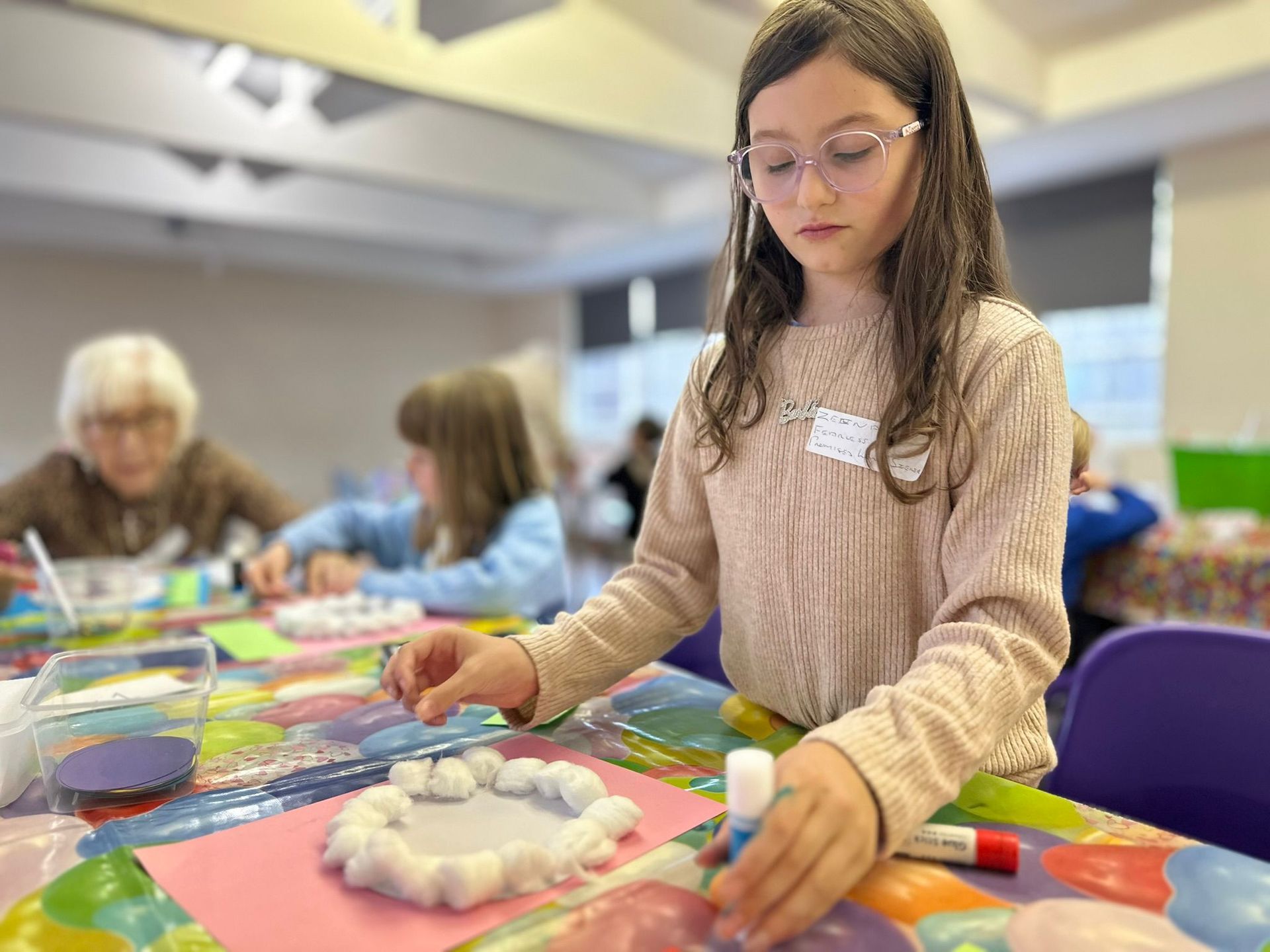 A young girl is sitting at a table making a craft with cotton balls.