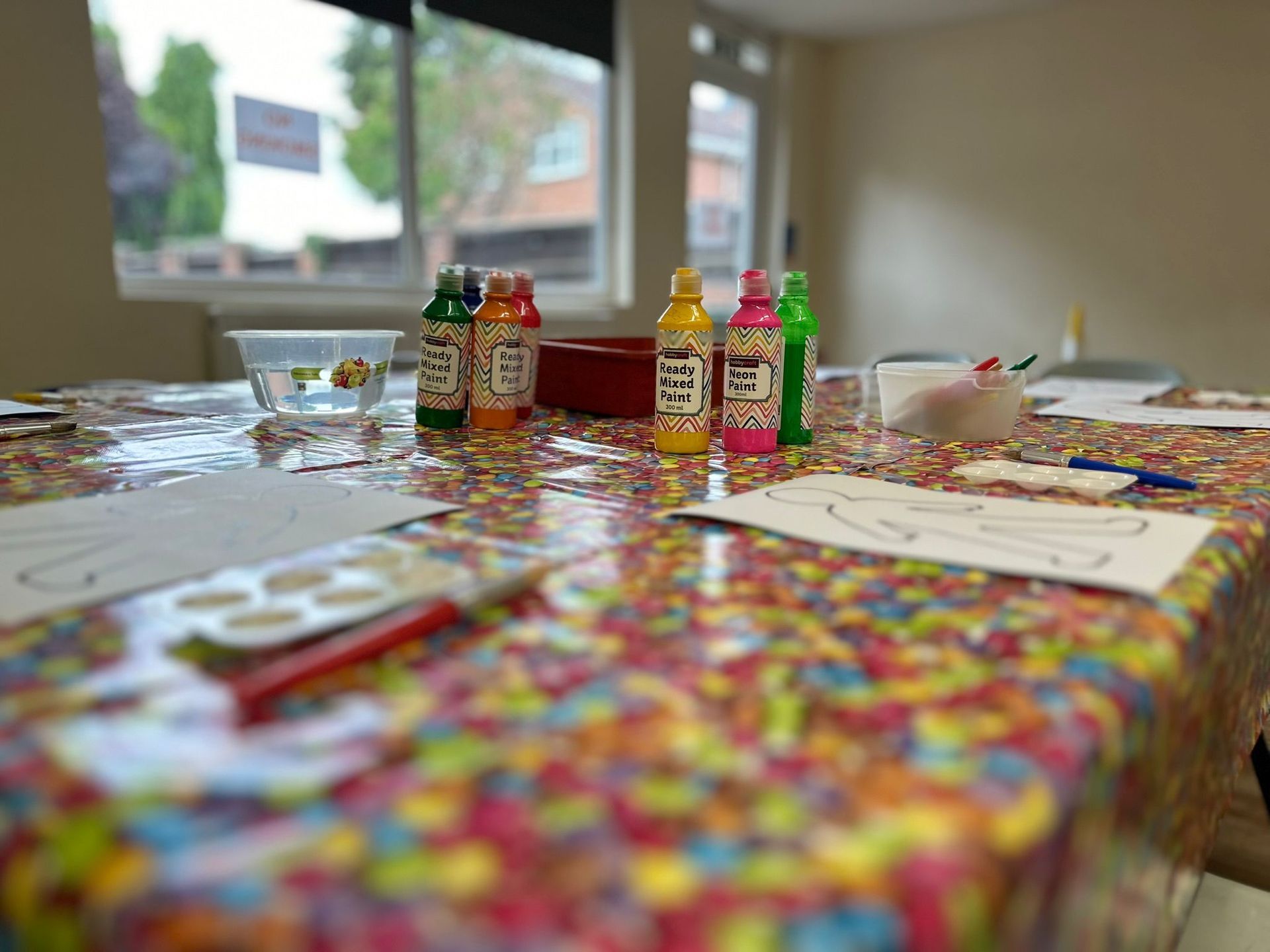 A table with a colorful tablecloth and bottles of paint on it.