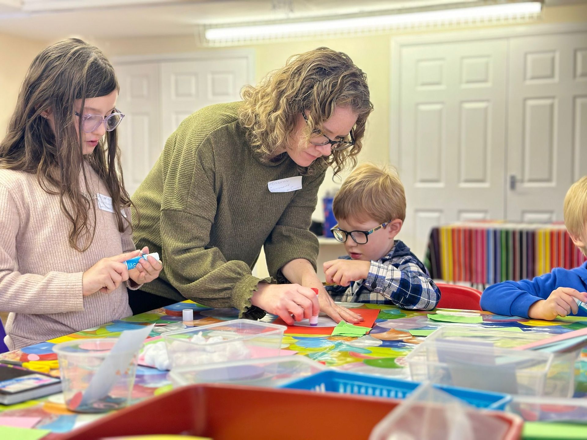 A woman is helping a group of children with crafts at a table.