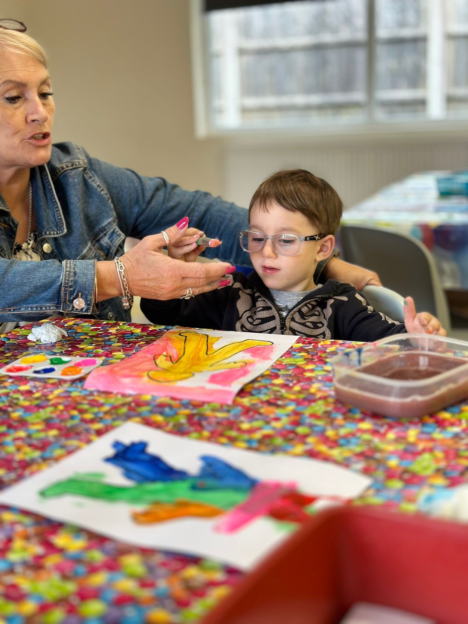 A woman is teaching a young boy how to paint at a table.