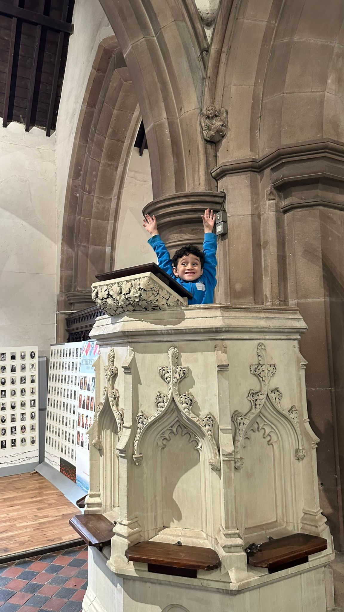 A young boy is sitting on a podium in a church with his arms in the air.