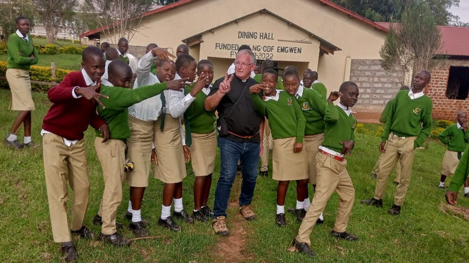 A group of children are posing for a picture with a man in front of a building.