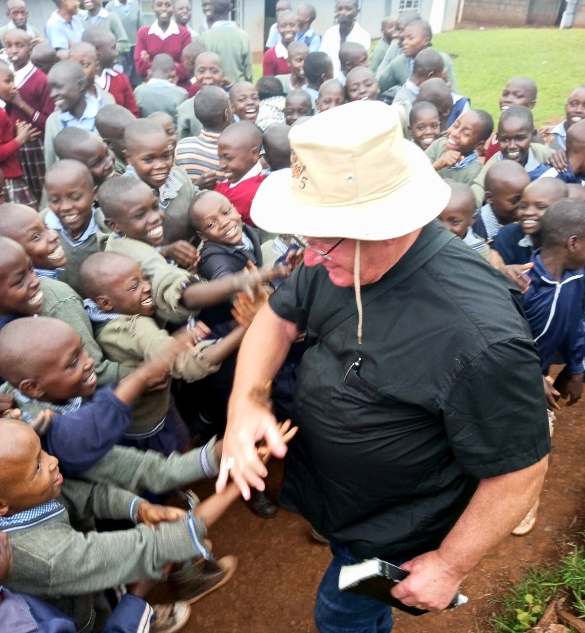 A man in a hat stands in front of a crowd of children