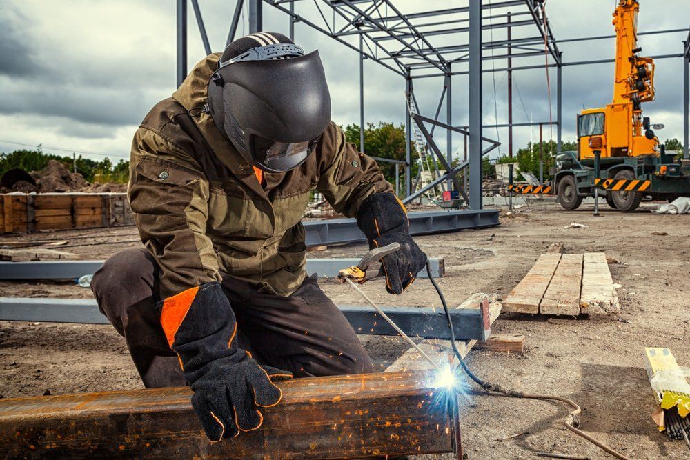 A Man Is Welding a Piece of Metal on A Construction Site — Mayric Engineering in Hallidays Point, NSW