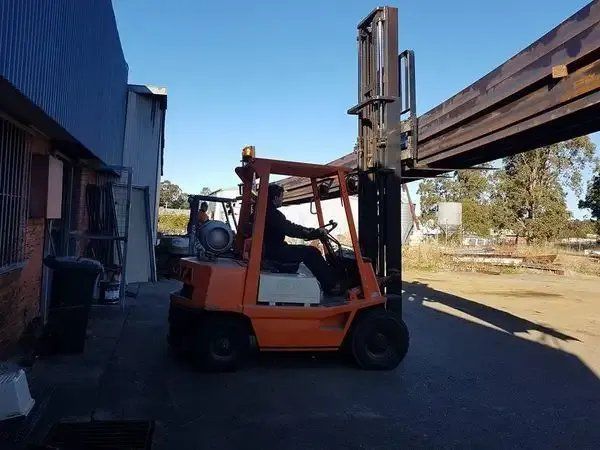 A Man Is Driving an Orange Forklift in A Parking Lot  — Mayric Engineering in Wingham, NSW