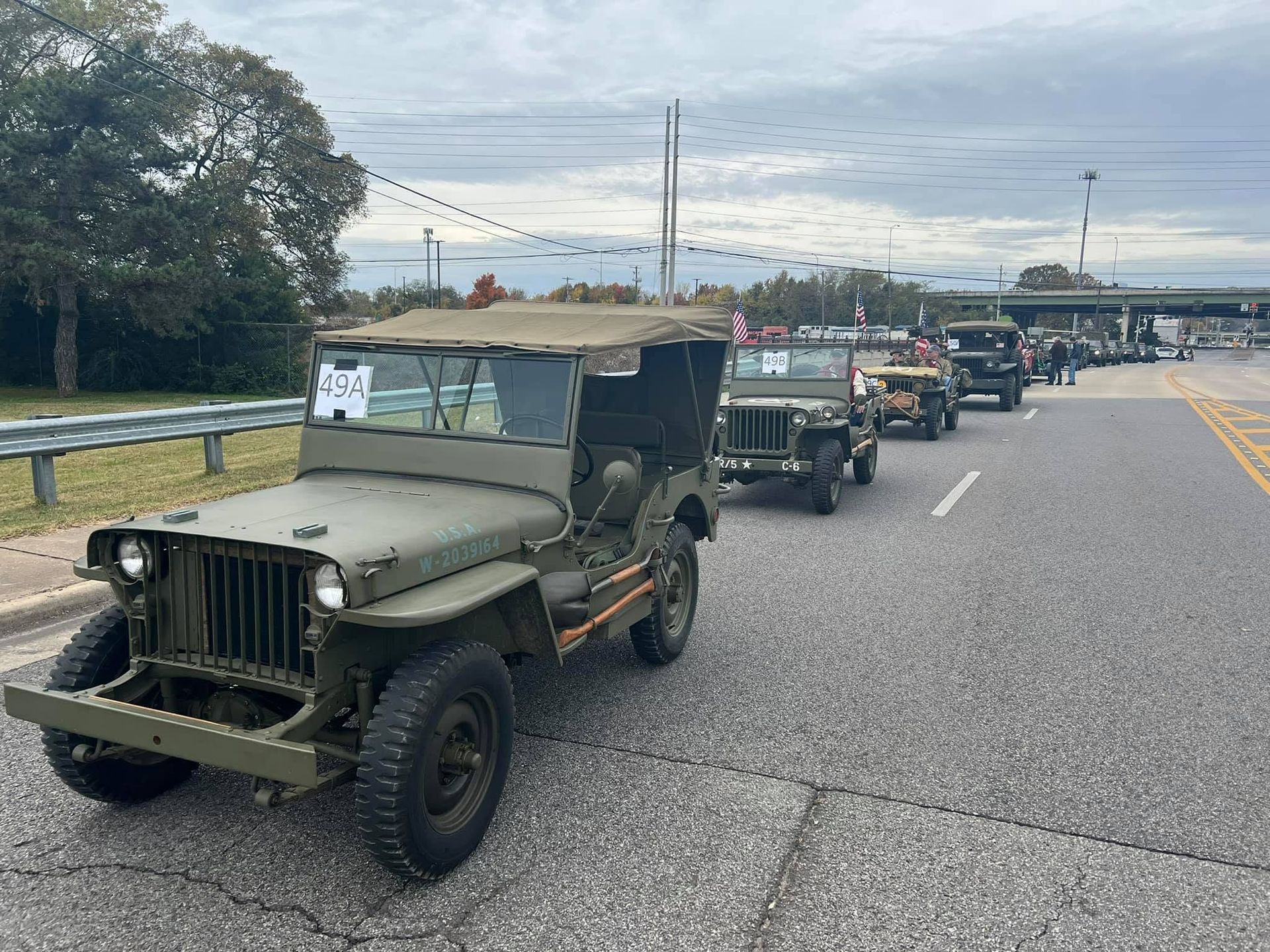 Military jeeps lined up on a road, with an olive-green jeep in the foreground under a cloudy sky.