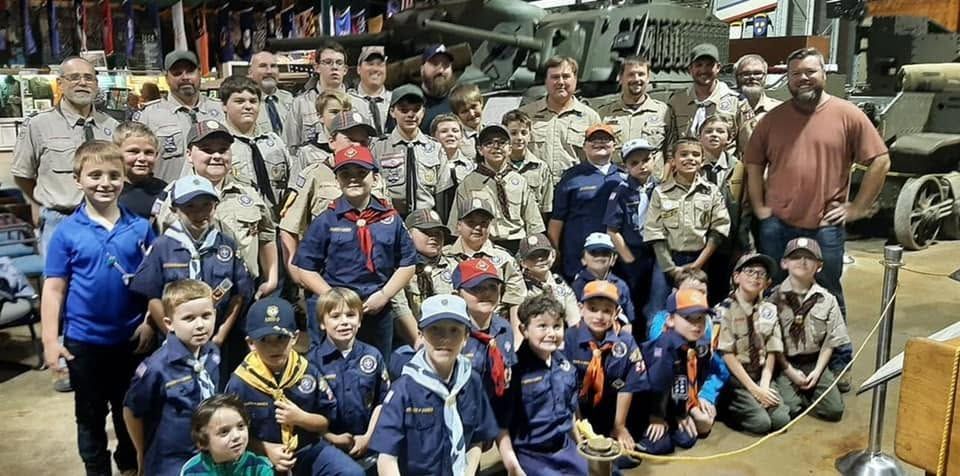 Large group posed in front of an aircraft, many wearing blue scout-style uniforms and caps