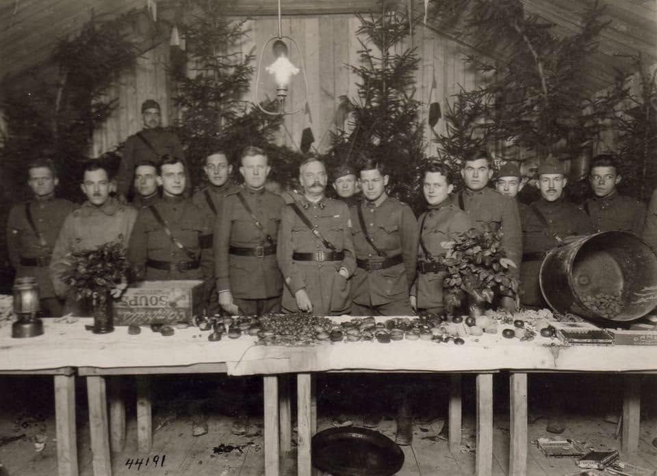Group of uniformed soldiers posing behind a table with flowers and a large drum in a decorated room.