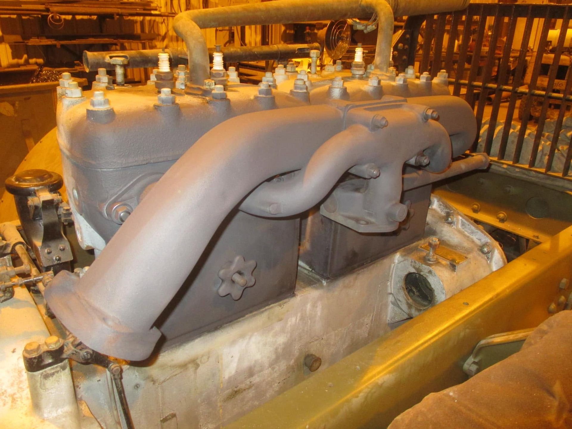 Large industrial engine with gray pipes and valves in a factory setting, lit by warm indoor lights