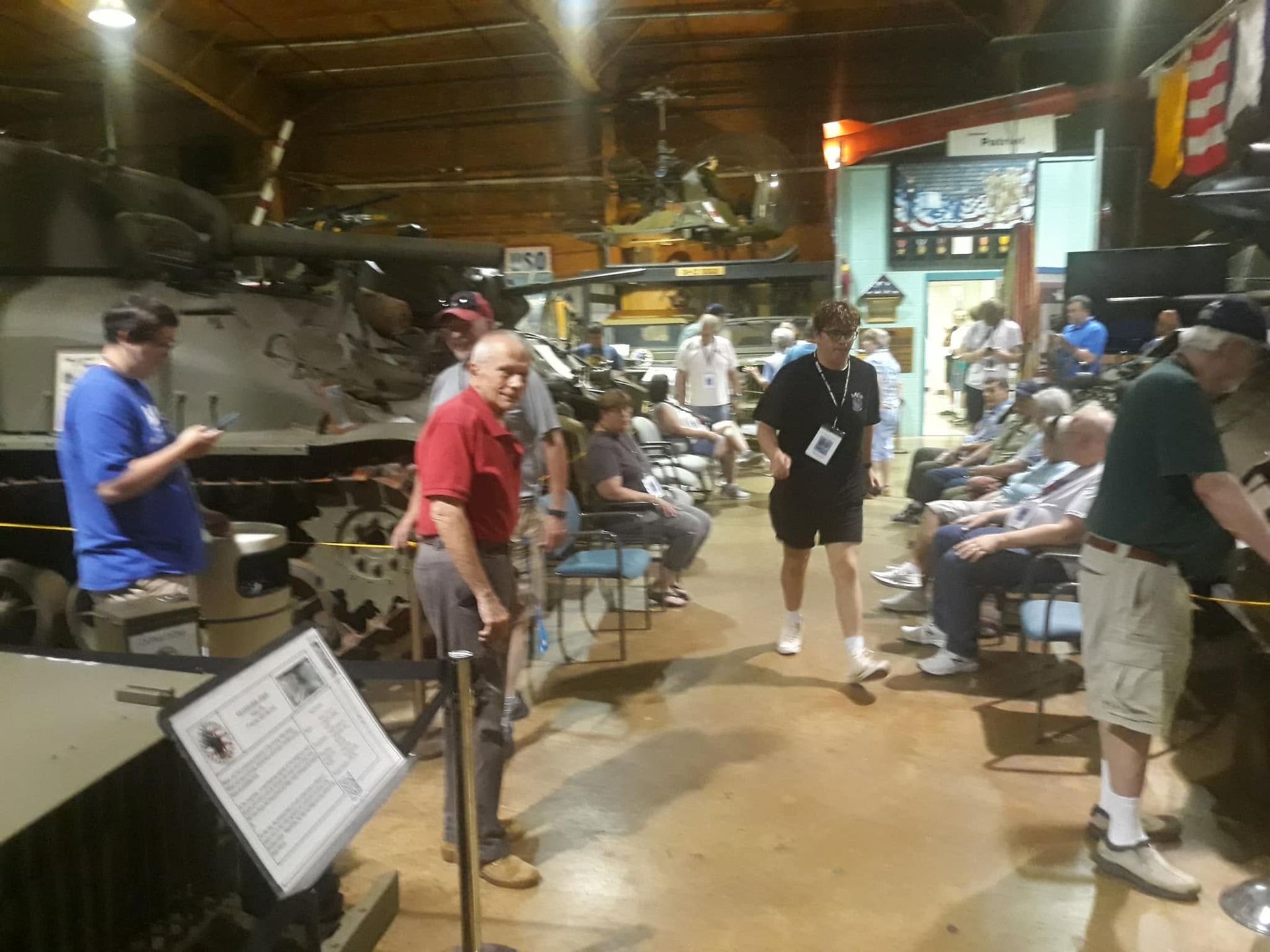 People seated in a rustic indoor venue, with a man in a red shirt standing near the center.