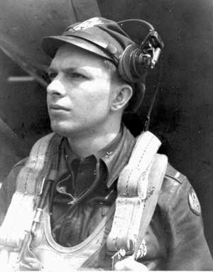 Black-and-white portrait of a pilot wearing a headset, cap, and flight gear, looking left.