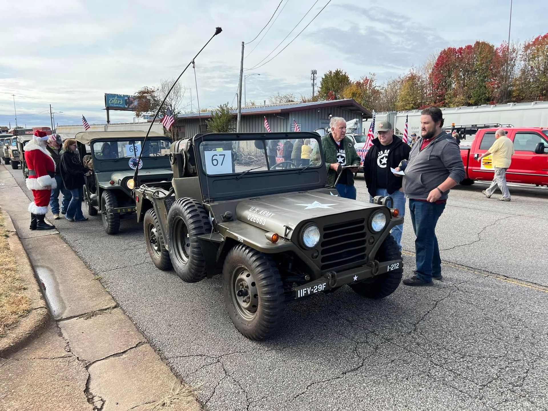 Old military jeep with number 57 parked on a road, with people standing nearby at a roadside event