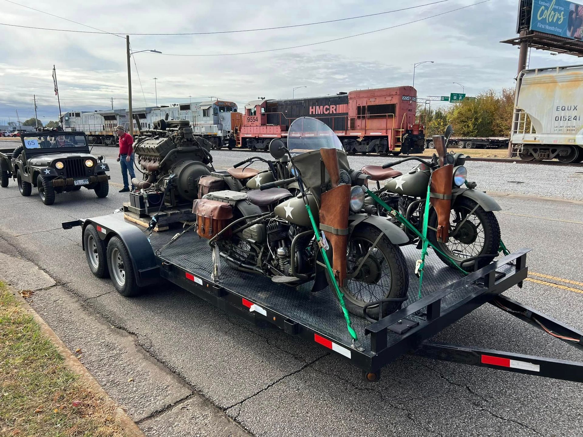 Overturned motorcycle on a trailer after a crash, with green tie-down straps on a roadside.