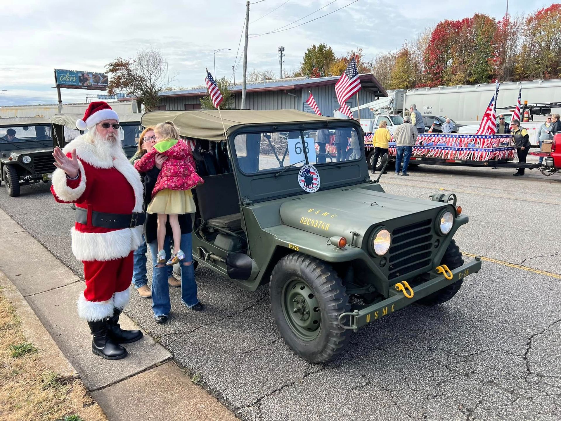 Santa and a child pose beside a decorated military jeep at a holiday parade