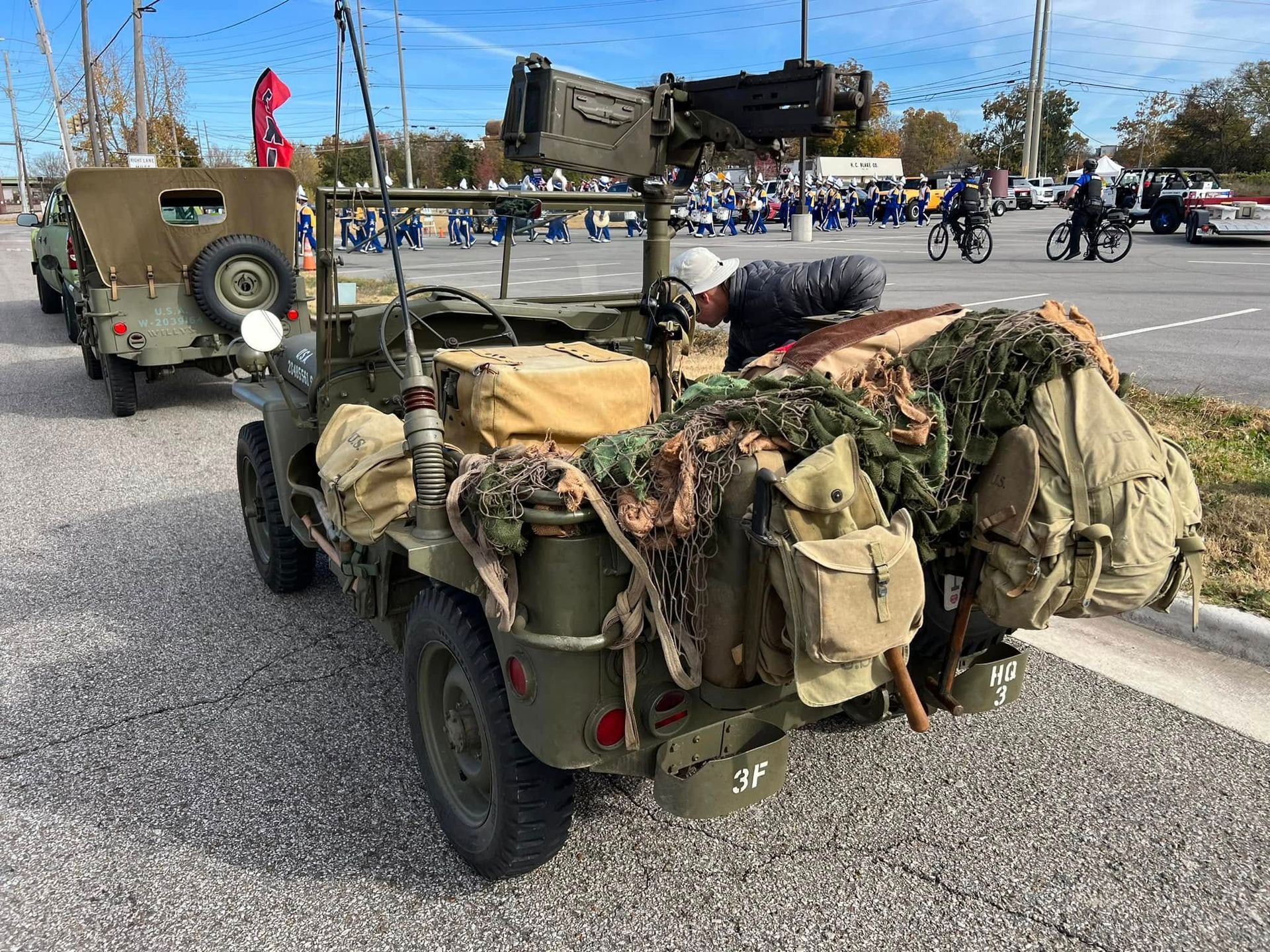 Military cargo trailer loaded with gear and tarps at a roadside parade or display.