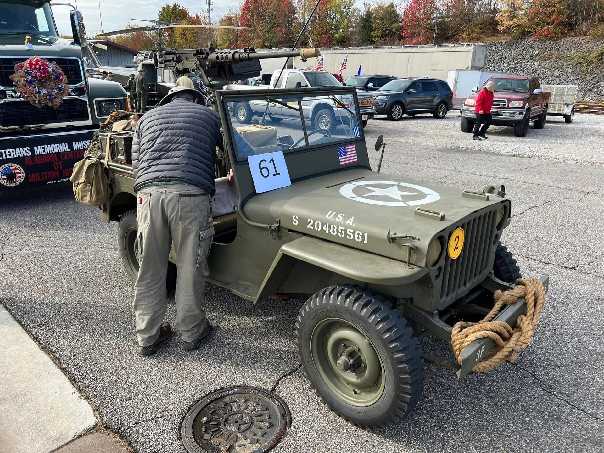 Man in vest standing beside an olive drab vintage jeep at an outdoor car show