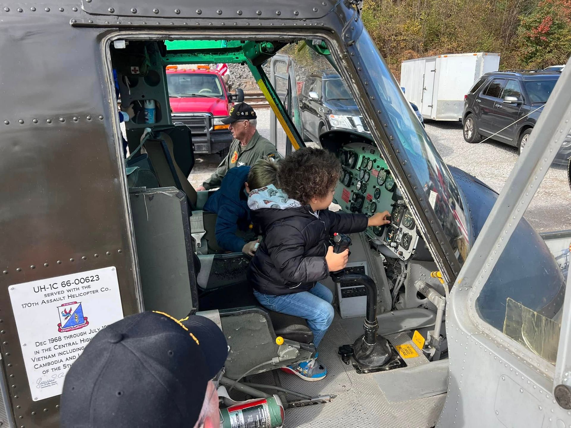 People seated in a helicopter cockpit, with one person operating the controls and the door open.