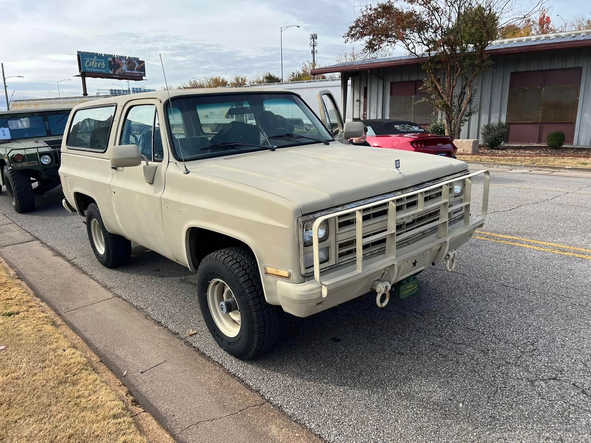 Beige vintage SUV parked on a street curb beside a building under a cloudy sky.