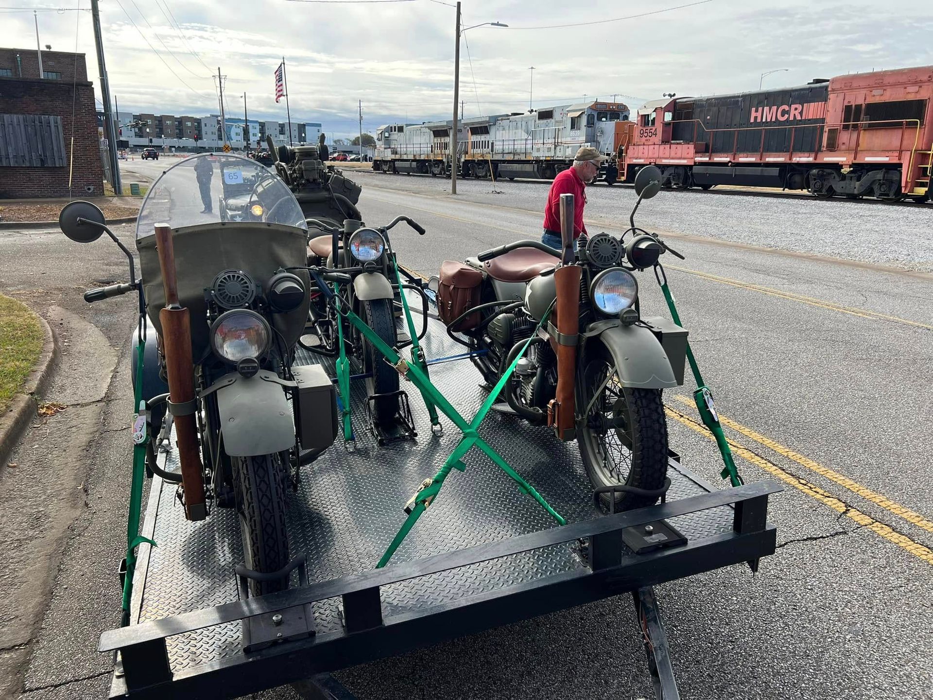 Three vintage motorcycles strapped on a flatbed trailer in an industrial rail yard