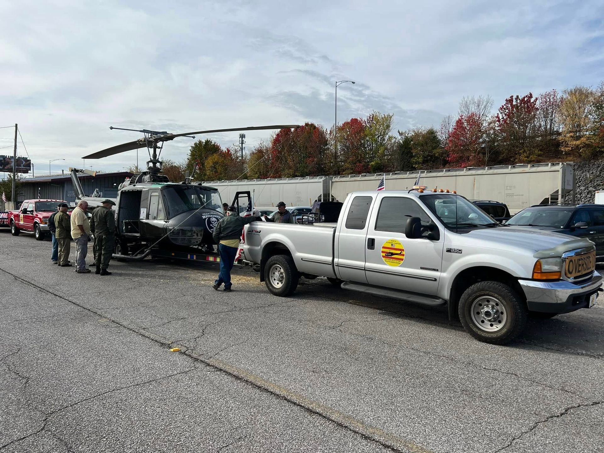Tow truck and silver pickup beside a police helicopter on a roadside with responders nearby