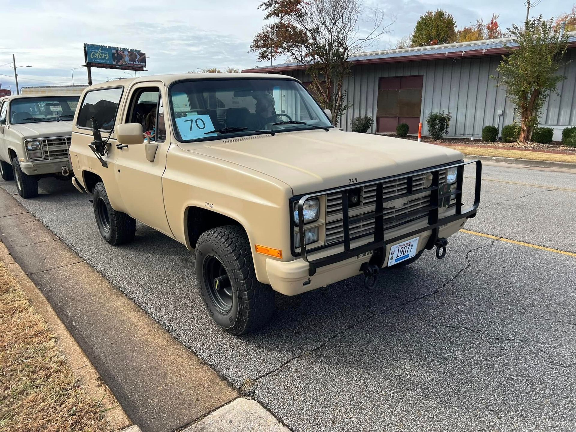 Beige pickup truck with brush guard parked on a roadside beside a white building