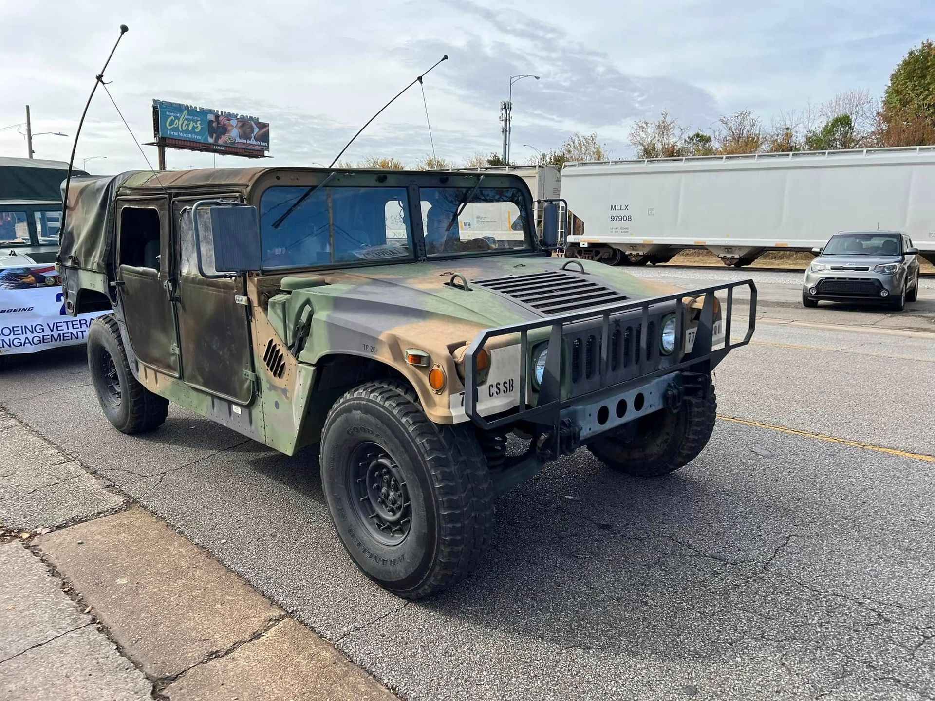 Camouflaged military Humvee parked on a city street beside a semi-truck trailer.