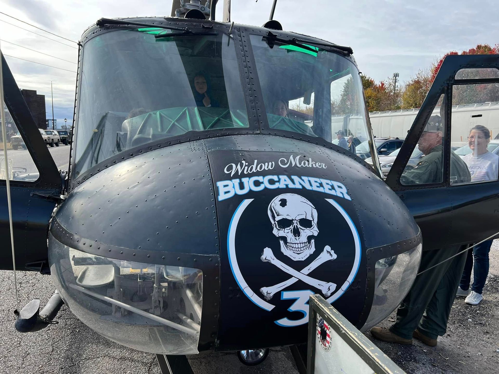 Black bus with pirate skull and crossbones logo on the front, doors open in a parking lot.