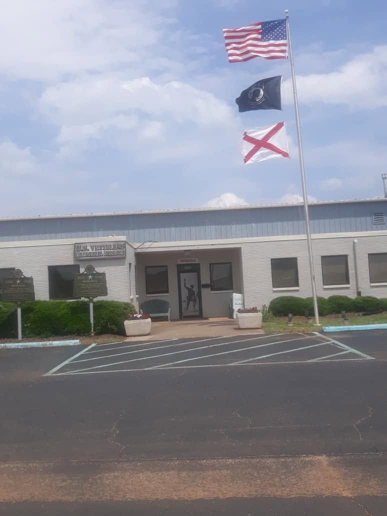 Building entrance with three flags flying on poles in front of it under a partly cloudy sky
