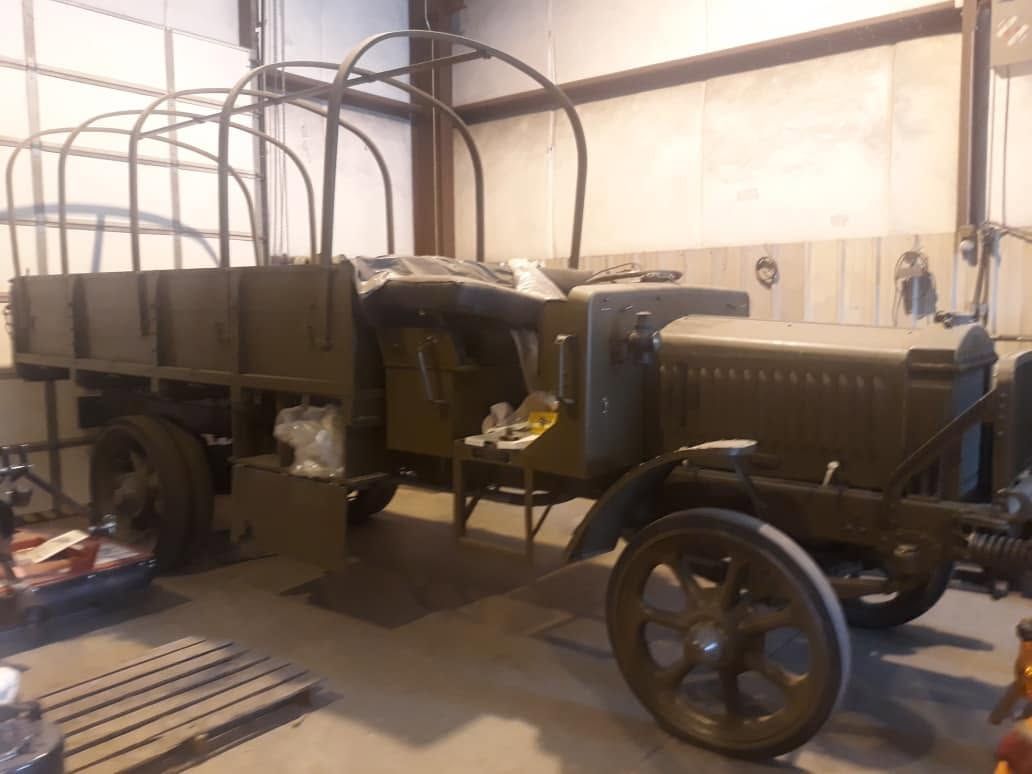 Vintage military truck in a warehouse, shown in side view with black body and large spoked wheels.