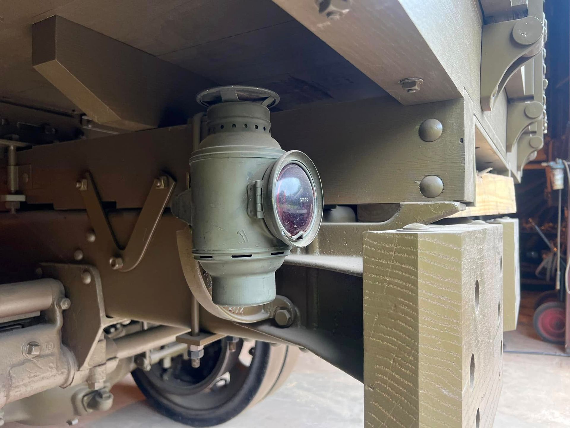 Close-up of a military vehicle’s mounted side light on tan metal armor near a wheel.