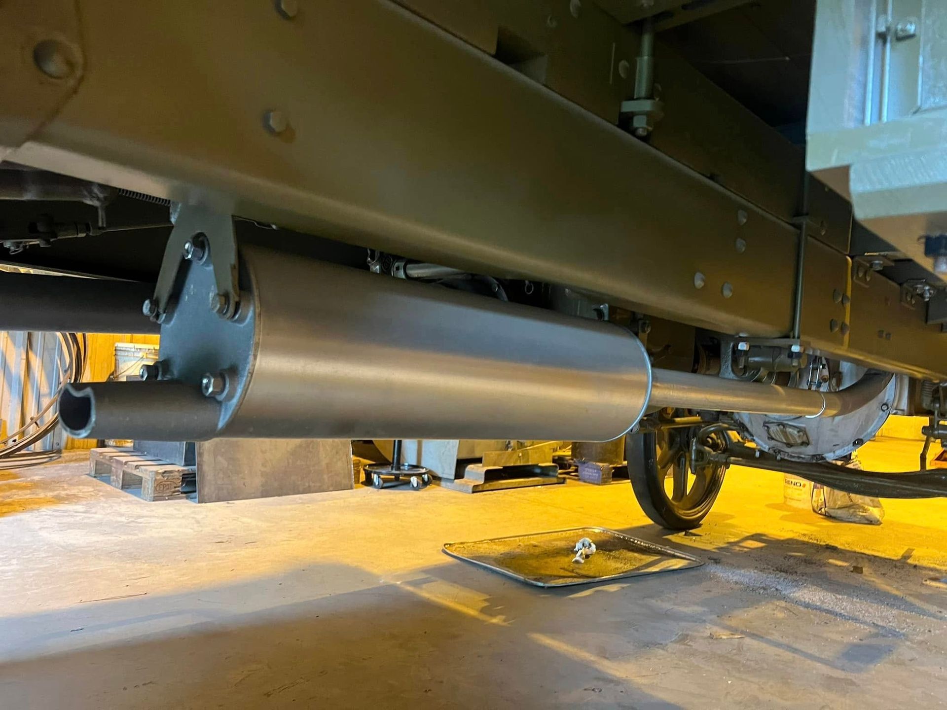 Undercarriage of a vehicle with a silver cylindrical exhaust tank and wheel on a sandy surface