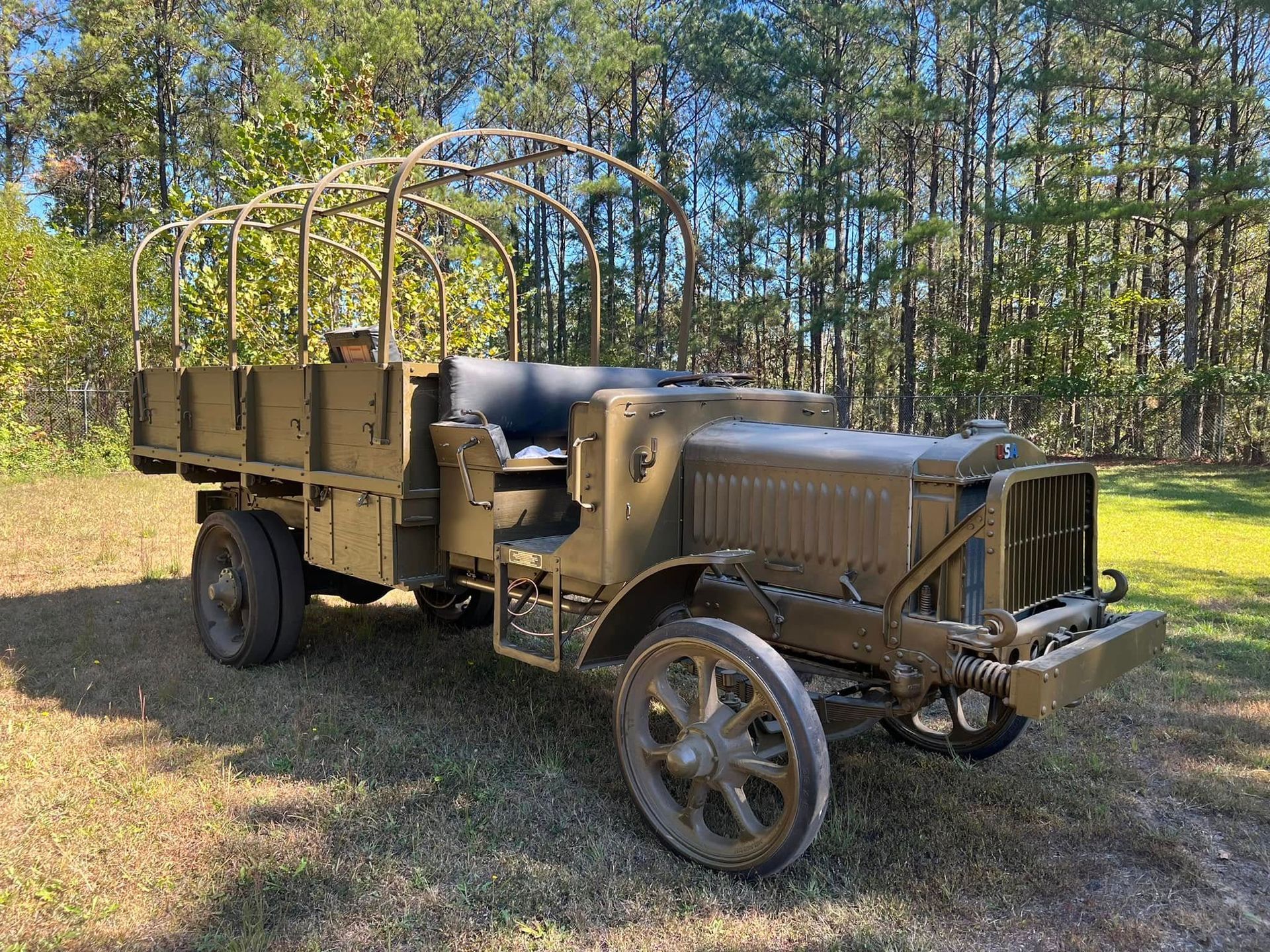 Vintage military truck parked on grass beside trees, with tan body and canvas-covered cargo bed.