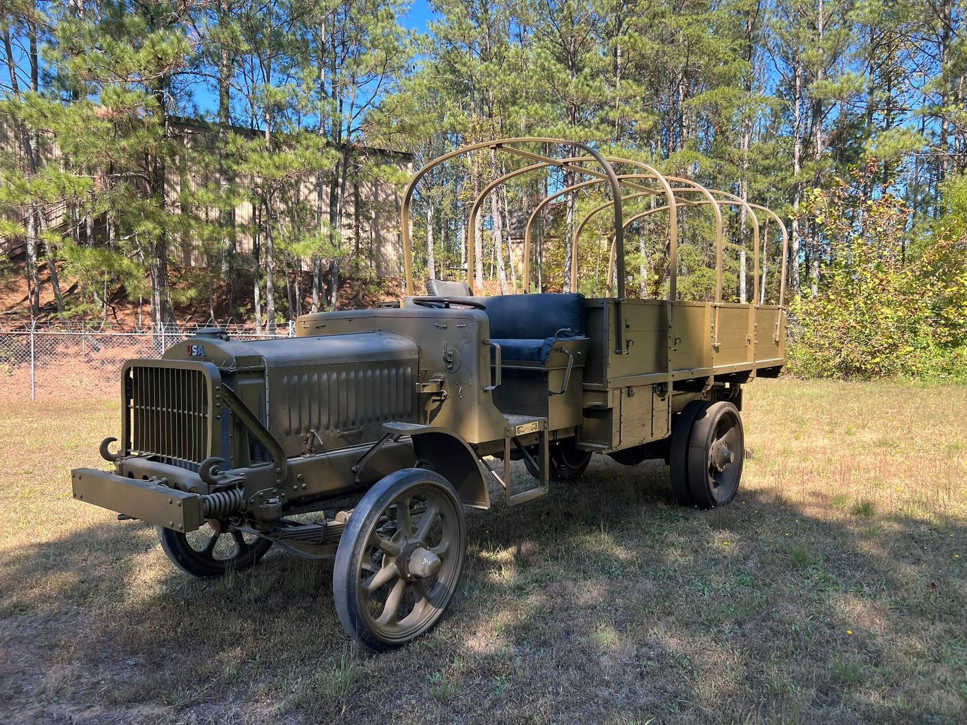 Vintage military truck in a grassy clearing with trees in the background.