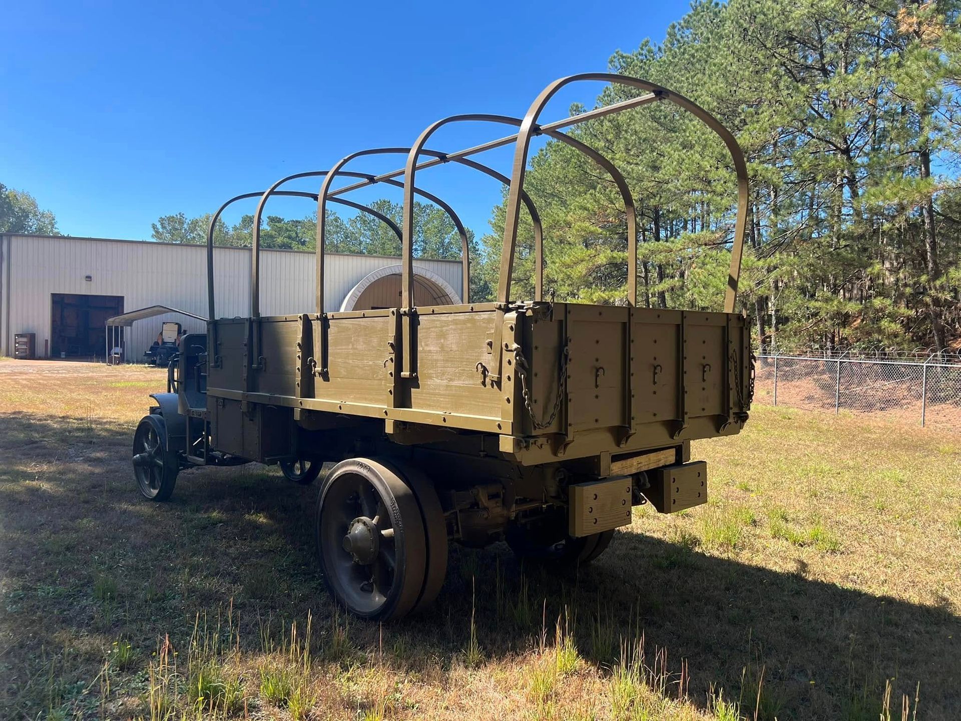 Vintage flatbed trailer with arched metal frame parked on grass beside a metal building and trees