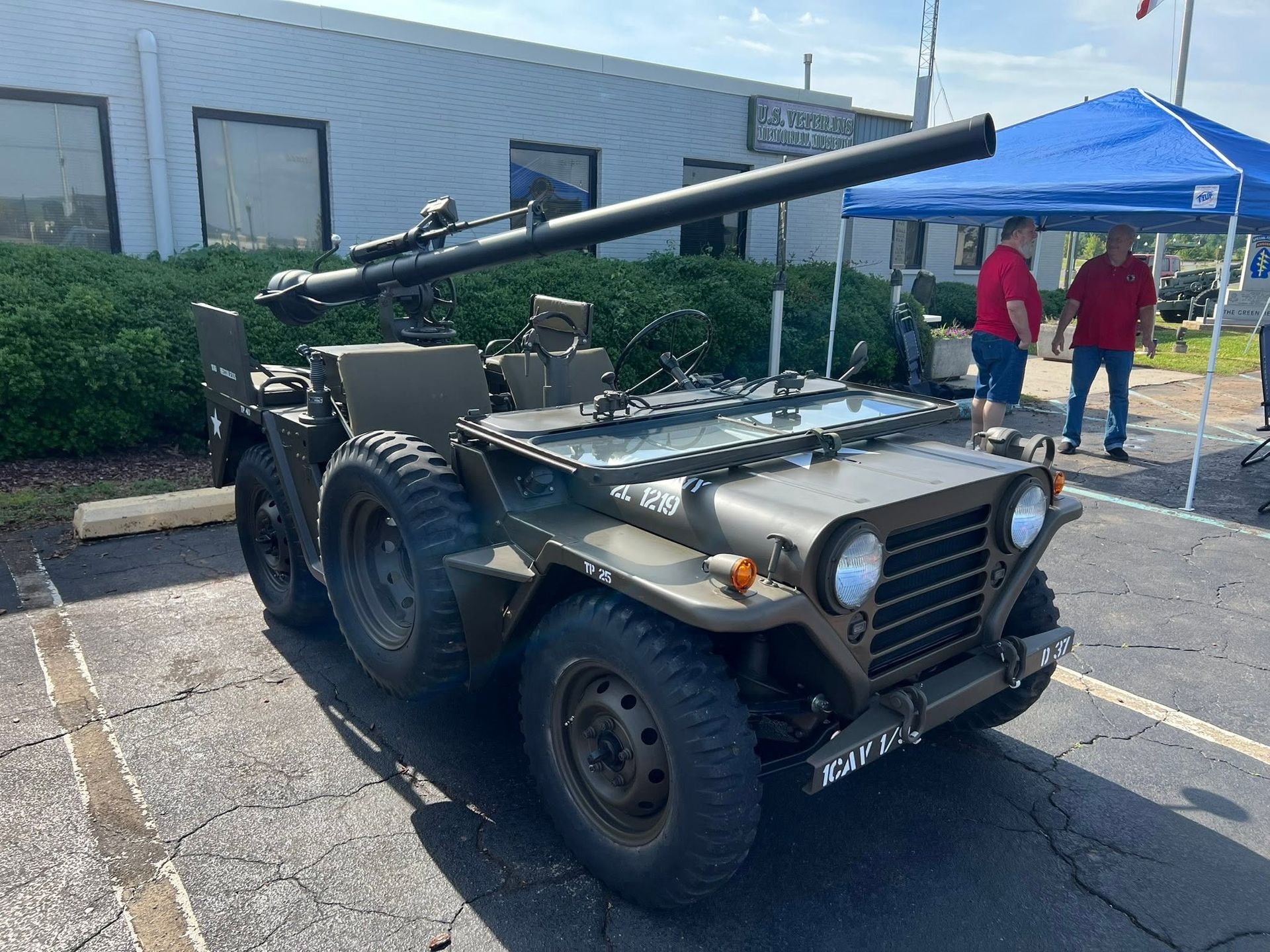 Vintage military jeep with a mounted cannon displayed outdoors on a parking lot.