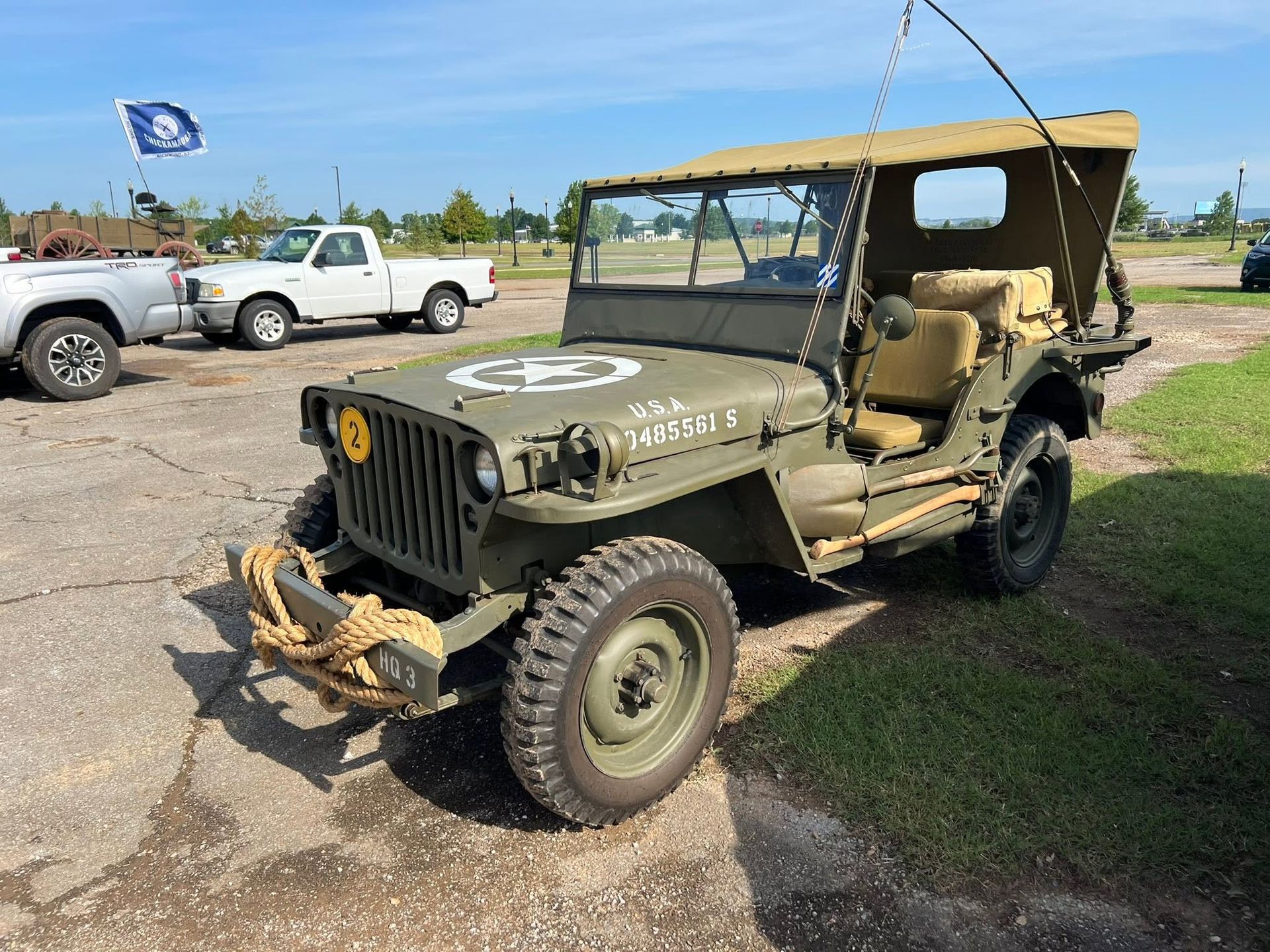 Olive drab vintage military Jeep parked outdoors on a gravel lot under a canopy.