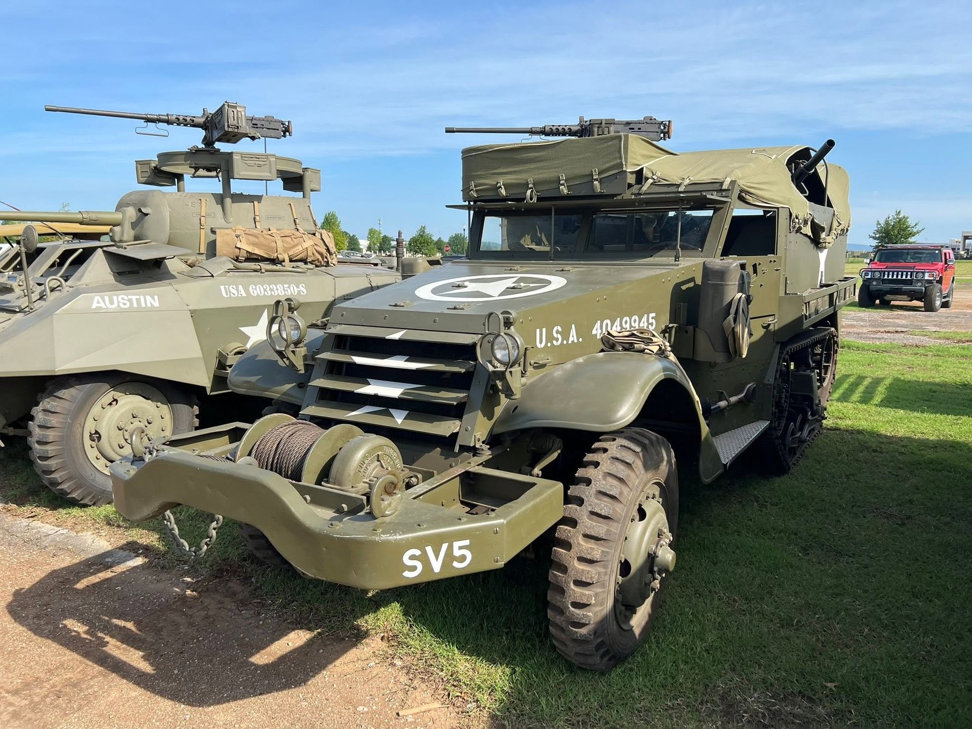 Two olive-drab military vehicles on grass, including an armored car with a mounted machine gun.