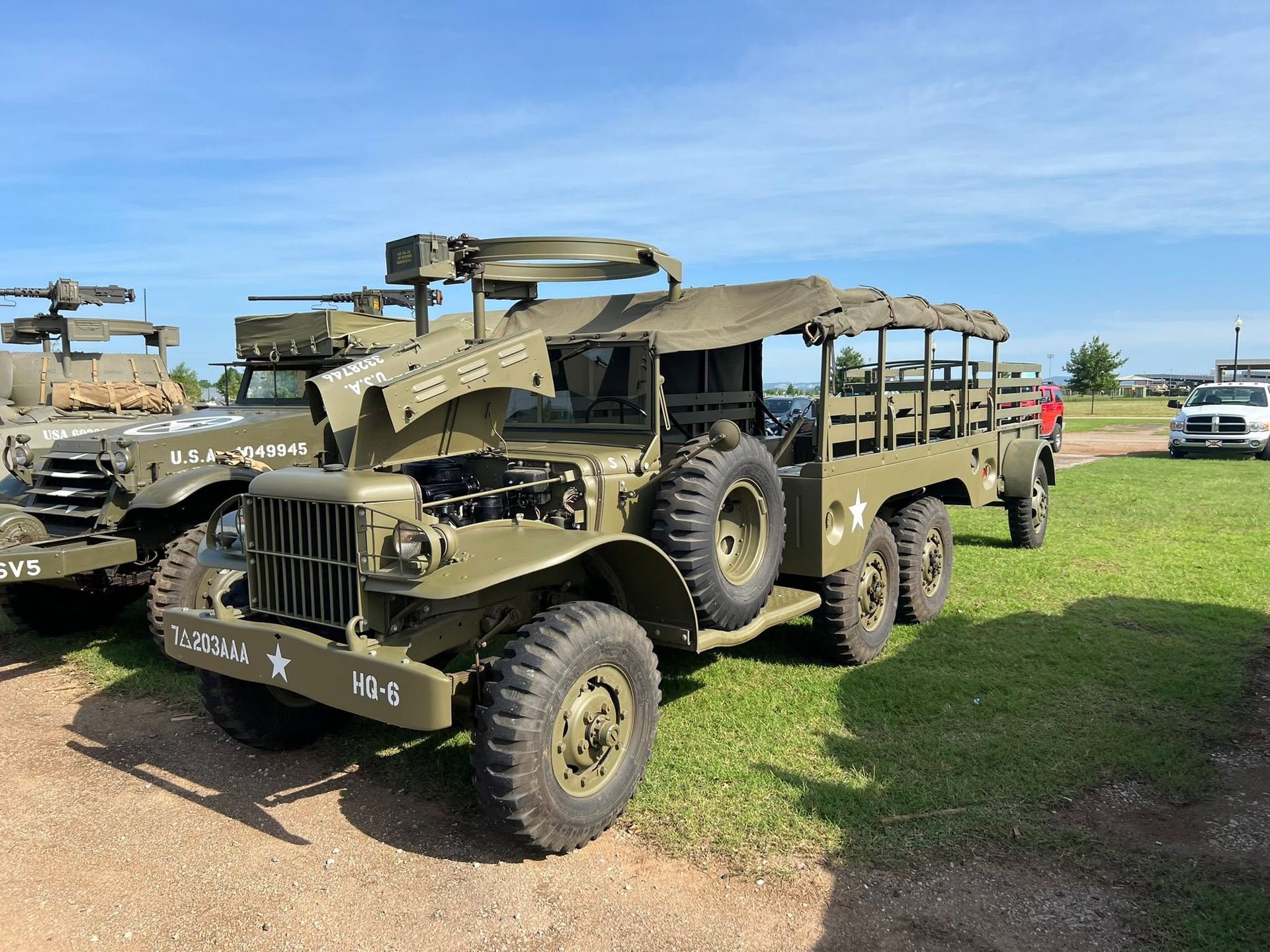 Military trucks and armored vehicles parked on grass under a clear blue sky.