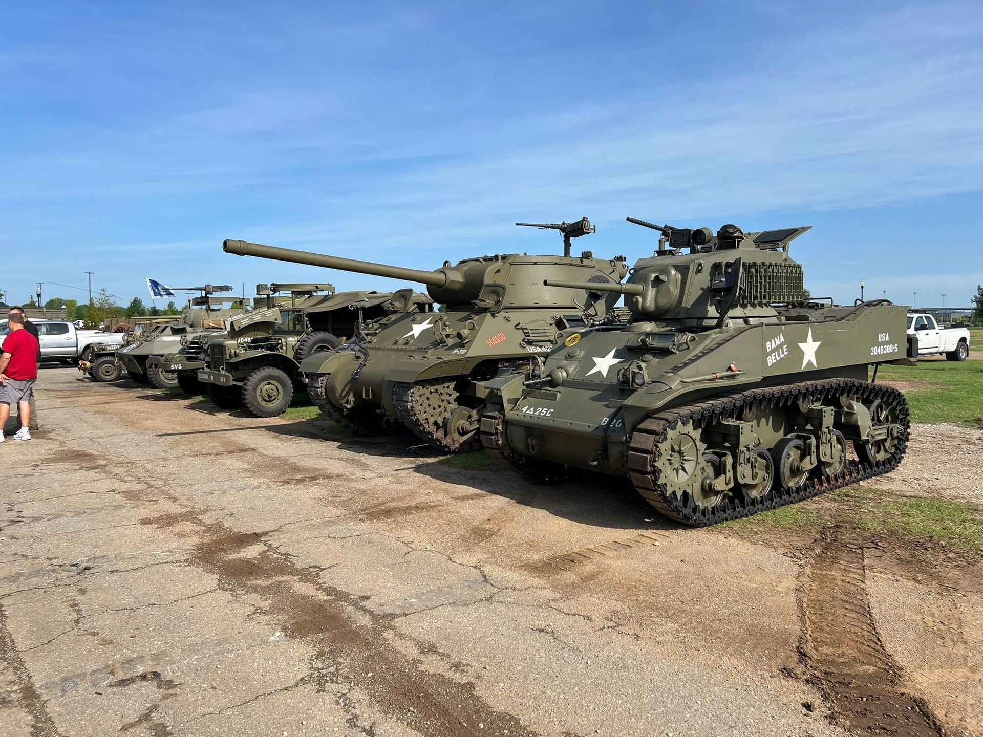 Military tanks lined up on a roadside under a clear blue sky, with soldiers nearby