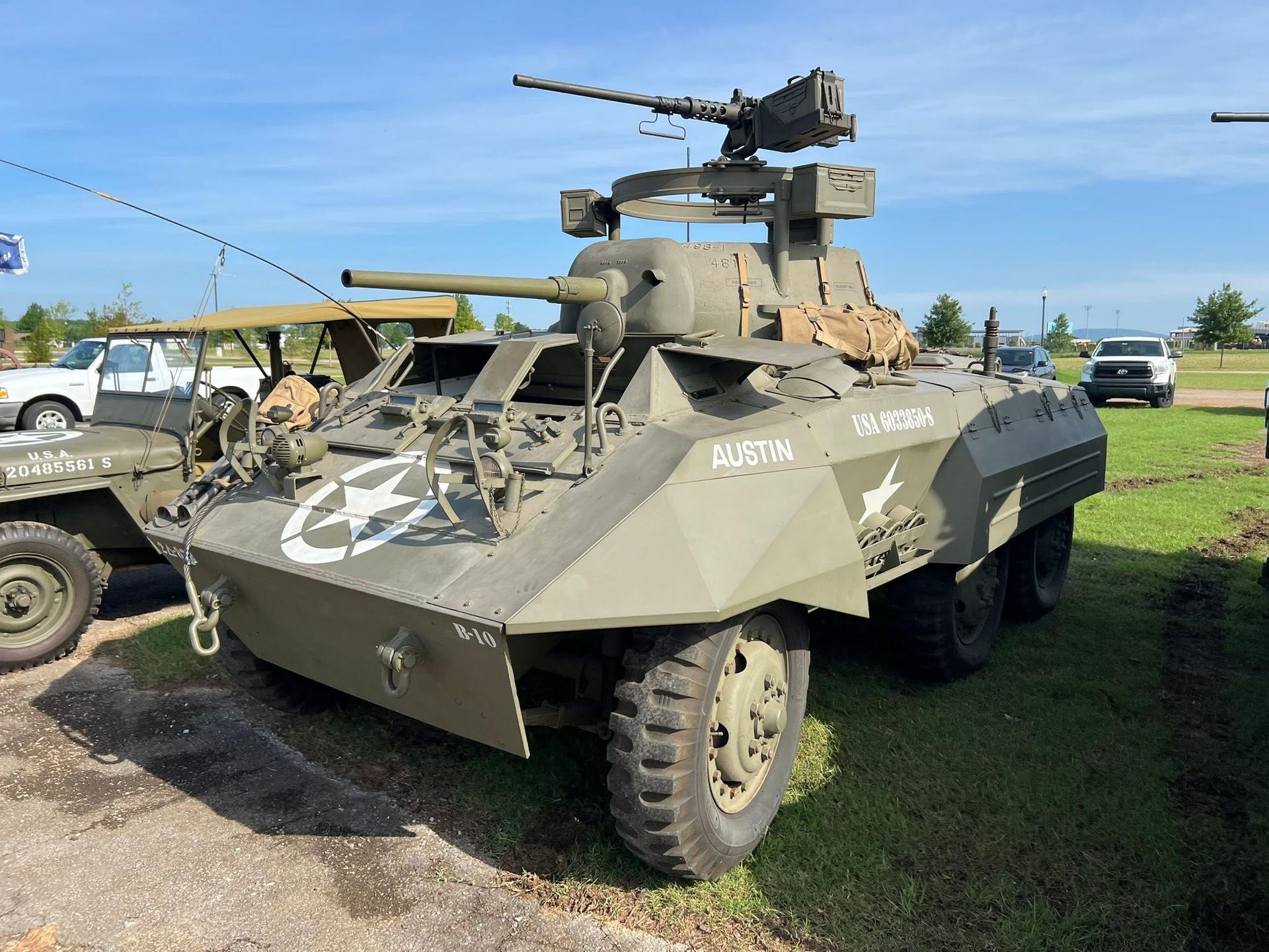 Camouflaged armored vehicle with mounted gun parked on grass under a blue sky