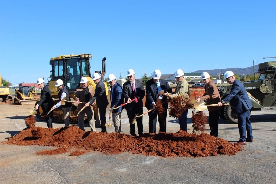 Workers in hard hats shoveling dirt at a construction site beside a backhoe under a clear blue sky