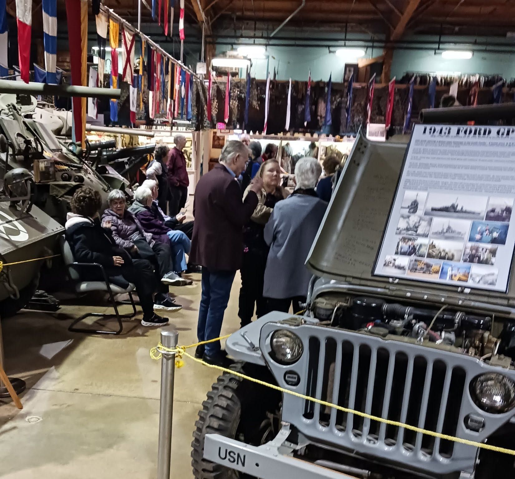 Vintage Jeep in a crowded museum, with visitors browsing military uniforms and gear in the background.